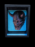 Decorative mask with horns in a dark frame against a black background