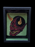 Framed artwork of a demon-like mask with horns on a green background