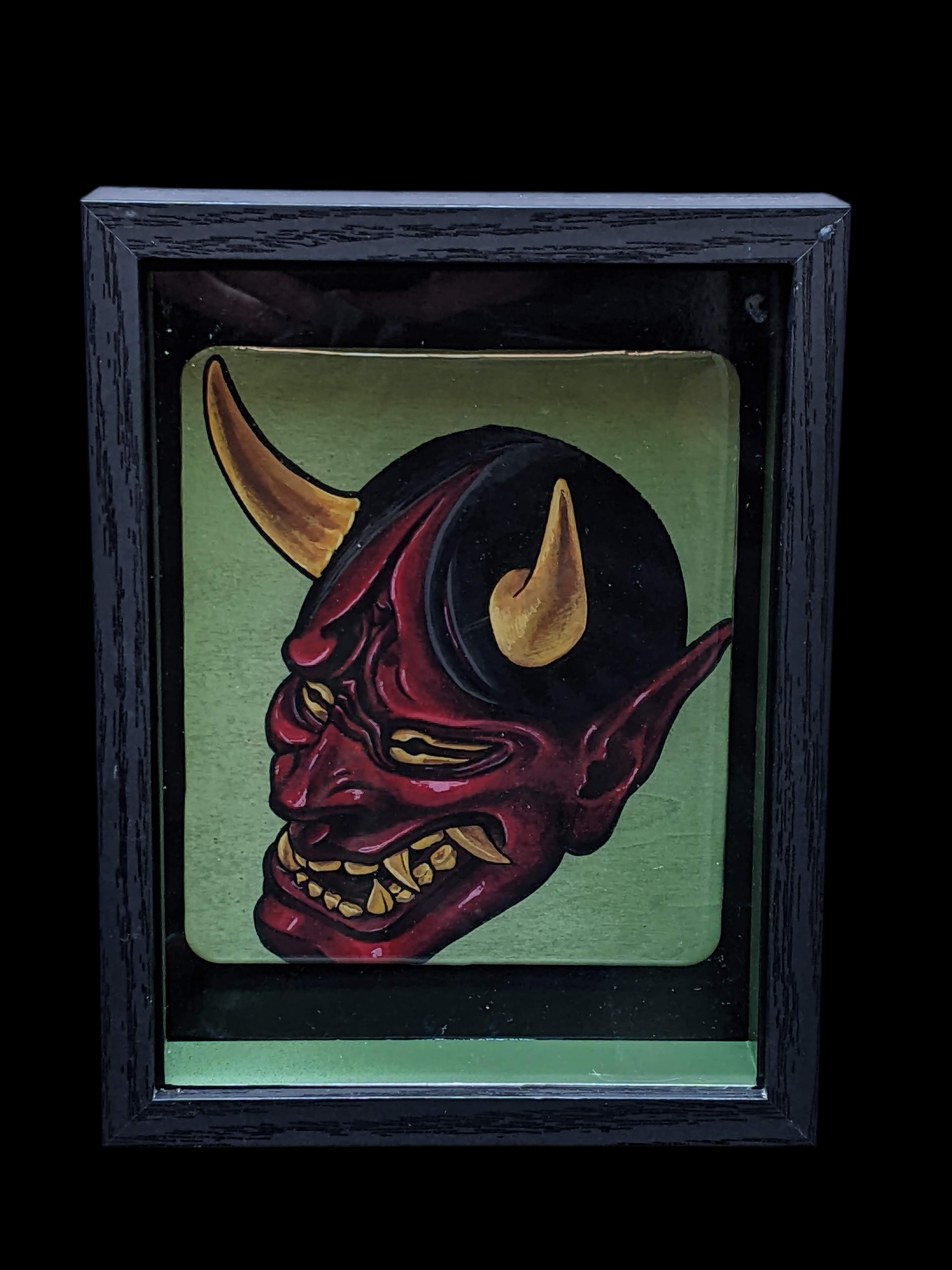 Framed artwork of a demon-like mask with horns on a green background