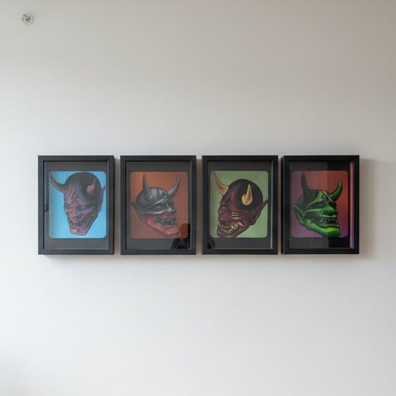 Four framed, shadow-box style art pieces are displayed side-by-side in a horizontal row on a plain white wall. Each frame contains a detailed, three-dimensional depiction of a traditional Japanese Hannya mask, set against a vibrant, contrasting background.