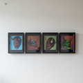 Four framed, shadow-box style art pieces are displayed side-by-side in a horizontal row on a plain white wall. Each frame contains a detailed, three-dimensional depiction of a traditional Japanese Hannya mask, set against a vibrant, contrasting background.