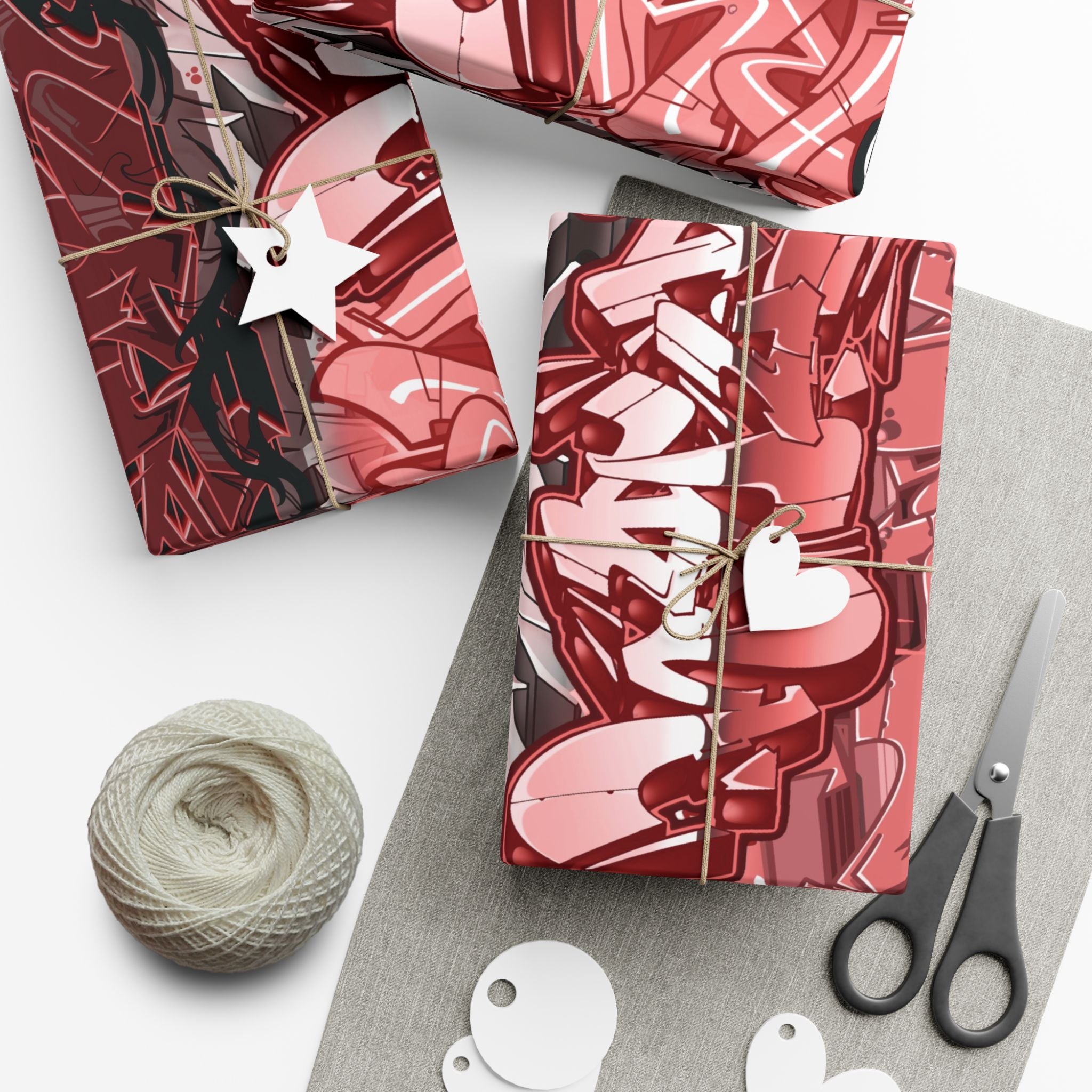 Red and pink patterned gift boxes with ribbons, scissors, and yarn on a white surface.