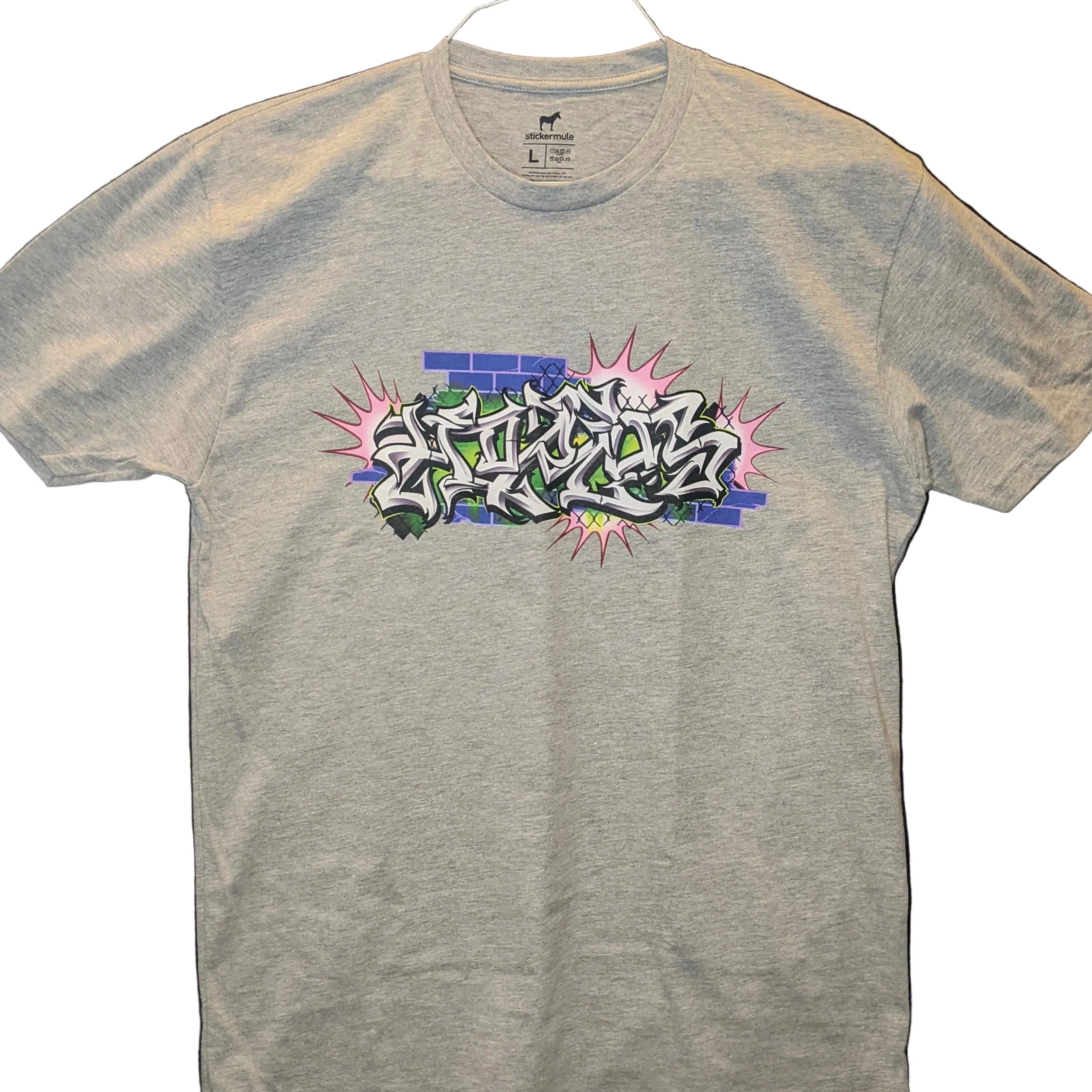 A heather grey crewneck t-shirt featuring a custom hand-style graffiti piece by Horus in silver, black, and lime green with a purple brick background and pink bursts